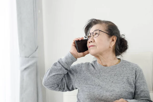 Asyalı yaşlı kadın ho kanepede oturan beyaz bir telefon görüşmesi yapmak — Stok fotoğraf