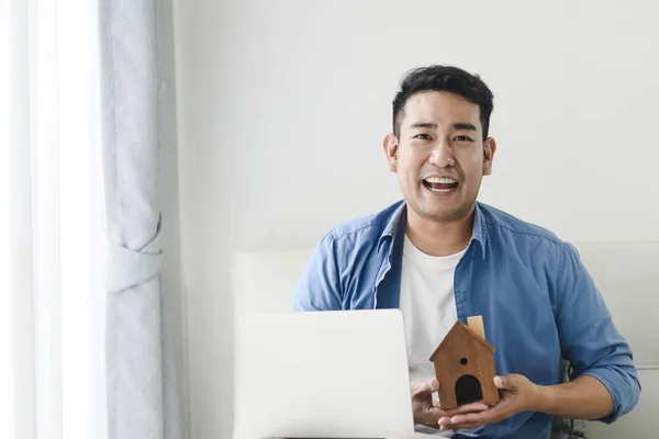 Asiatique homme tenant maison dans sa main et en utilisant un ordinateur portable, immobilier — Photo