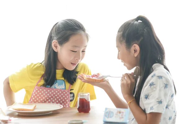 Irmã asiática espalhando geléia de morango no pão para sua irmã mais nova . — Fotografia de Stock