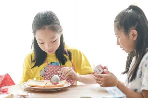 Aziatische zuster spreiden aardbei jam op brood voor haar jongere zus. — Stockfoto