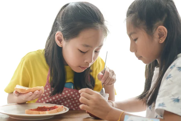 Asijská Sestra rozšiřuje jahodovou marmeládu na chleba pro mladší s — Stock fotografie