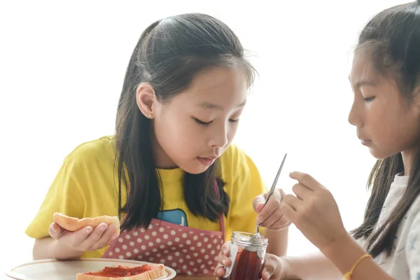 Asiatische Schwester Verbreitung Erdbeermarmelade auf Brot für Ihr jüngeres s — Stockfoto