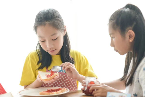 Aziatische zuster spreiden aardbei jam op brood voor haar jongere s — Stockfoto