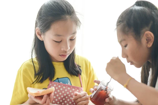 Asiatische Schwester Verbreitung Erdbeermarmelade auf Brot für Ihr jüngeres s — Stockfoto