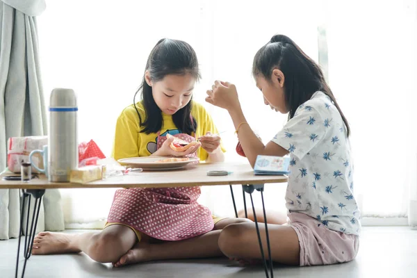 Asiatico sorella diffusione fragola marmellata su pane per il suo più giovane s — Foto Stock