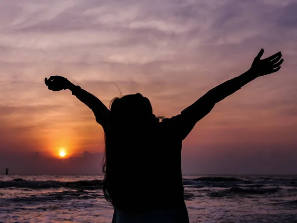 Menina levantando as mãos com o nascer do sol no fundo da praia . — Fotografia de Stock