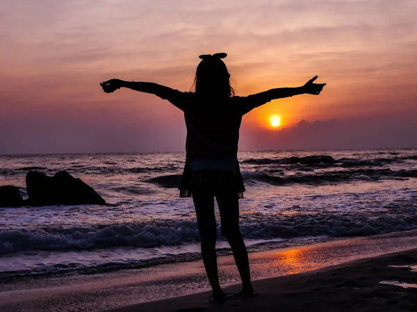 Menina levantando as mãos com o nascer do sol no fundo da praia . — Fotografia de Stock