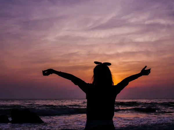 Menina levantando as mãos com o nascer do sol no fundo da praia . — Fotografia de Stock