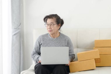 Packag ile online satış yaparken dizüstü bilgisayar kullanan Asyalı yaşlı kadın