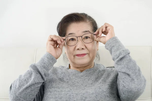 Lycklig asiatisk Senior kvinna klädd i glasögon och sitter på soffan — Stockfoto