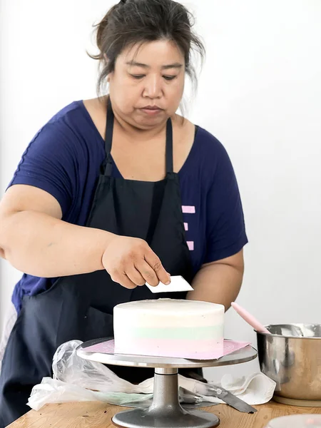 Asian woman spreading whie butter cream on homemade chocolate ca