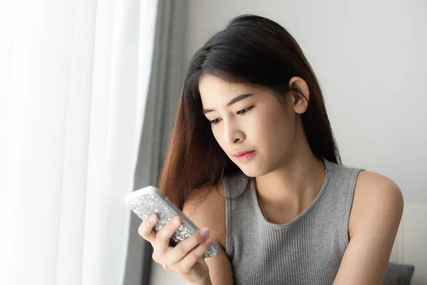 Asiatin entspannt sich auf Sofa und benutzt Smartphone zu Hause, das Leben — Stockfoto