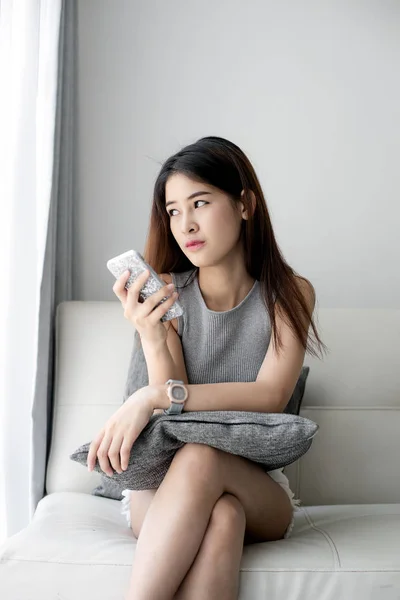 Asiatin entspannt sich auf Sofa und benutzt Smartphone zu Hause, das Leben — Stockfoto