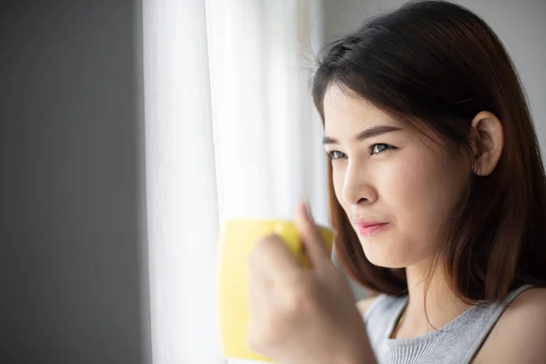 Femme asiatique tenant tasse jaune près de la fenêtre avec de la lumière naturelle . — Photo