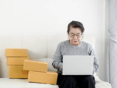 Packag ile online satış yaparken dizüstü bilgisayar kullanan Asyalı yaşlı kadın