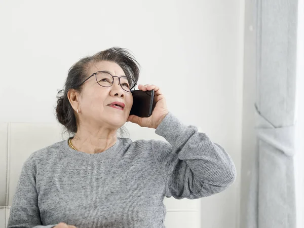 Азиатская старшая женщина делает телефонный звонок белый сидя на диване на хо — стоковое фото