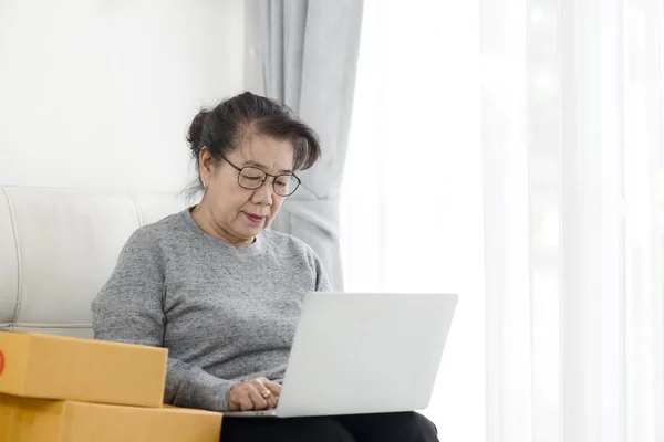 Азиатская старшая женщина использует ноутбук при продаже онлайн с пакетом — стоковое фото