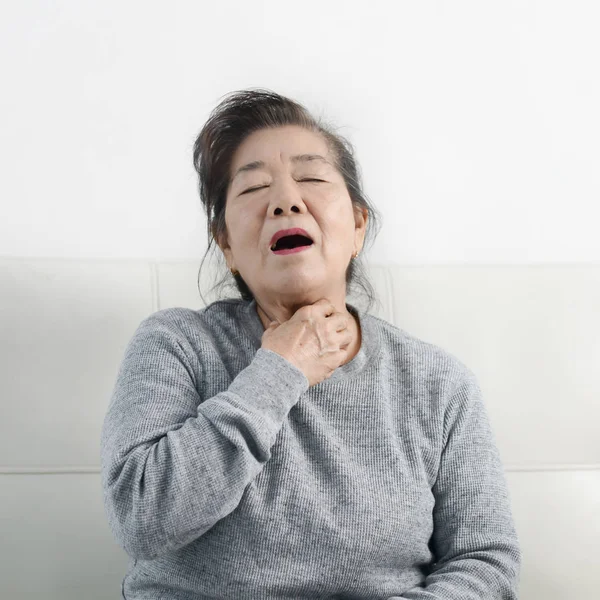 Ásia sênior mulher tem um tosse enquanto sentado no sofá, estilo de vida — Fotografia de Stock