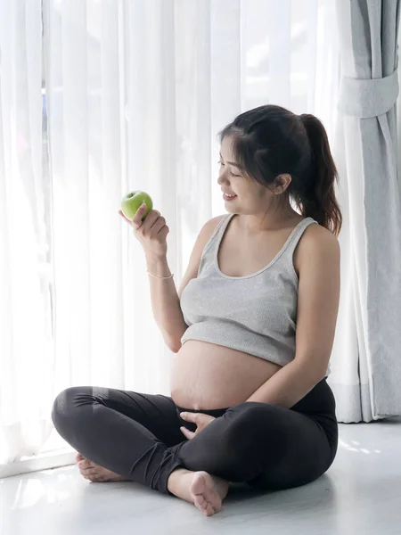 Счастливая азиатская женщина держит зеленое яблоко в руке и сидит на — стоковое фото