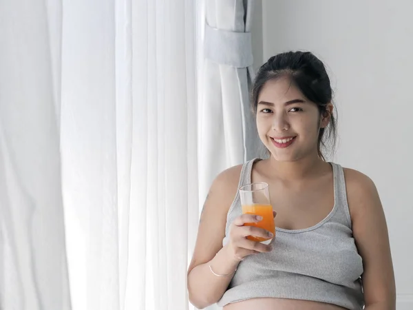 Беременная азиатка держит стакан апельсинового сока и стоя — стоковое фото