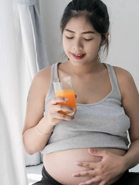 Asiático mulher grávida segurando um copo de suco de laranja e standin — Fotografia de Stock