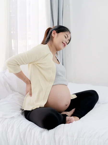Mulher asiática grávida com dor nas costas na frente de uma janela, saúde — Fotografia de Stock