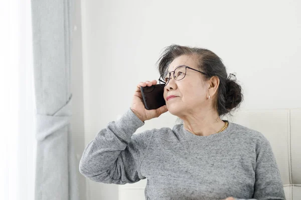 Asyalı yaşlı kadın ho kanepede oturan beyaz bir telefon görüşmesi yapmak — Stok fotoğraf