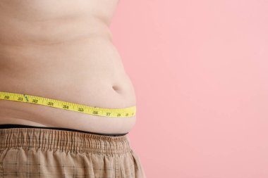 Pembe bir backgroun bir bant ölçüsü ile karnı ile Asyalı çocuk