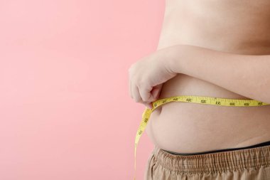 Pembe bir backgroun bir bant ölçüsü ile karnı ile Asyalı çocuk