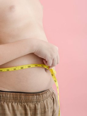 Pembe bir backgroun bir bant ölçüsü ile karnı ile Asyalı çocuk