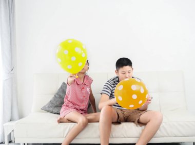 Asyalı kız kardeşi ve erkek kardeşi birlikte evde balon oynuyor, 