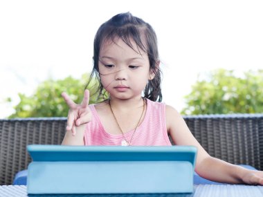 Asya kız doğa arka plan ile masada tablet kullanarak.