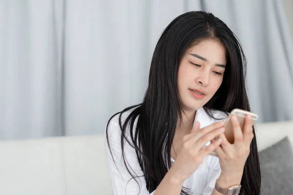 Mujer asiática relajándose en el sofá y usando el teléfono inteligente en casa, la vida — Foto de Stock