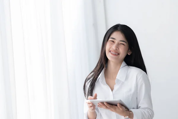 Mulher asiática bonita em camisa branca usando tablet perto da janela em — Fotografia de Stock