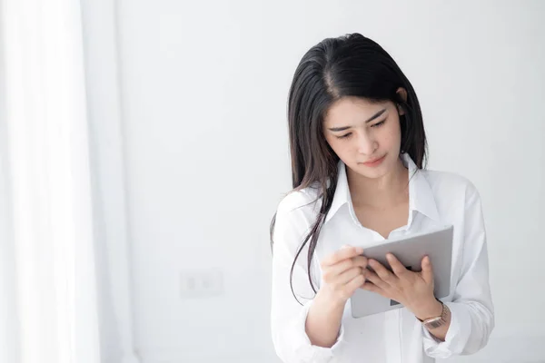 Piękna kobieta azjatyckich w białej koszuli przy użyciu tabletu w pobliżu okna w — Zdjęcie stockowe