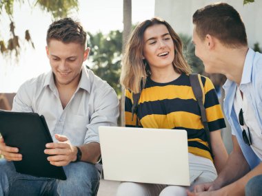 Mutlu üniversite öğrencisi bina dışında birlikte dizüstü bilgisayar kullanarak 