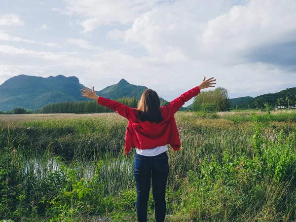 Back of woman wearing red jacket raising hand with nature view b — Stock Photo, Image