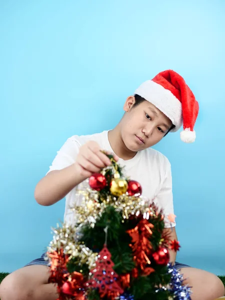 Asian boy wearing red santa hat decorating christmas tree, holid — Stock Photo, Image