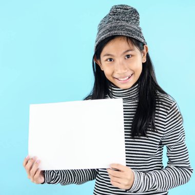 Mavi b üzerinde beyaz boş kağıt tutan kış kostümü Asyalı kız