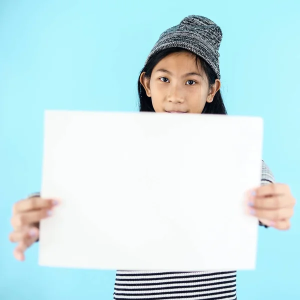 Asian girl in winter costume holding white blank paper on blue b — Stock Photo, Image