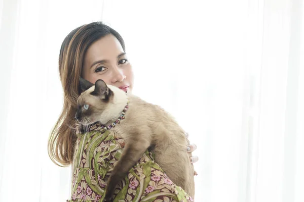 Gülümseyen Asyalı kadın kedisini pencere ışığıyla tutuyor.. — Stok fotoğraf