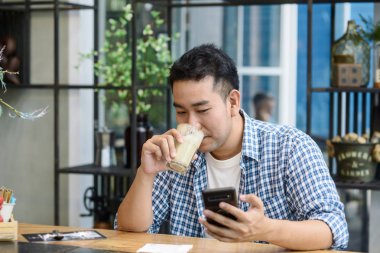 Zeki Asyalı adam kafede akıllı telefon kullanıyor ve kahve içiyor.
