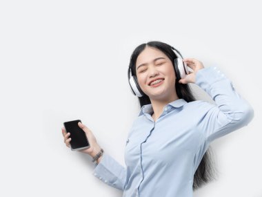 Mutlu Asyalı kadın akıllı telefon ve kulaklık kullanarak müzik dinliyor.