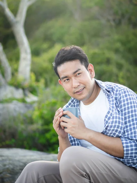 Asiático homem segurando xícara de café com natureza ao ar livre, estilo de vida conc — Fotografia de Stock