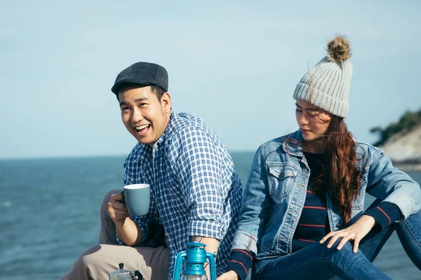 Happy Asian couple holding coffee cups on mountain peak together