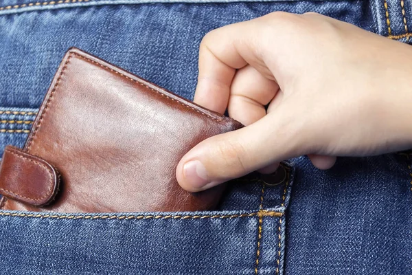 A hand pulls a wallet out of the back pocket of his jeans.The concept of pickpocketing or theft in the family from parents.