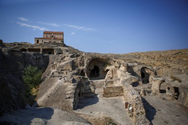 Georgia 'daki antik taş mağara şehri Uplistsikhe. Kahverengi taş, kavurucu güneşin altında çöldeki harabeler ve mağaralar. Taş evler, kilise, antik manzaralı sokaklar..
