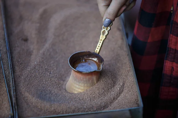 Manufacturing sand coffee in a copper cezve. Turkish coffee, Georgian coffee. Female hand holding a Turk with coffee over hot sand