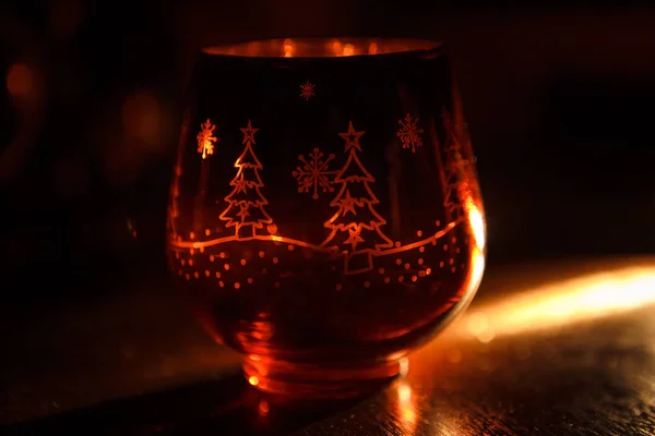 Glass candle holder with Christmas Christmas graphics in the form of the glass. Snowflakes, Christmas trees glow in the decorative candlestick inside yellow light. Festive Christmas decor.