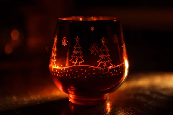 Glass candle holder with Christmas Christmas graphics in the form of the glass. Snowflakes, Christmas trees glow in the decorative candlestick inside yellow light. Festive Christmas decor.